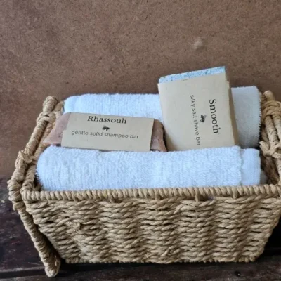 Rhassouli shampoo bar and Smooth shave bar in a basket with soft white towels.