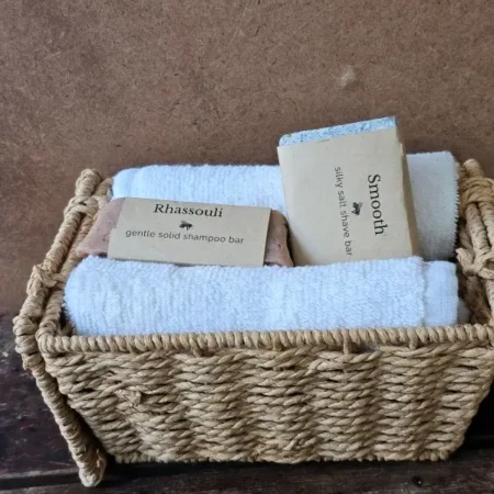 Rhassouli shampoo bar and Smooth shave bar in a basket with soft white towels.