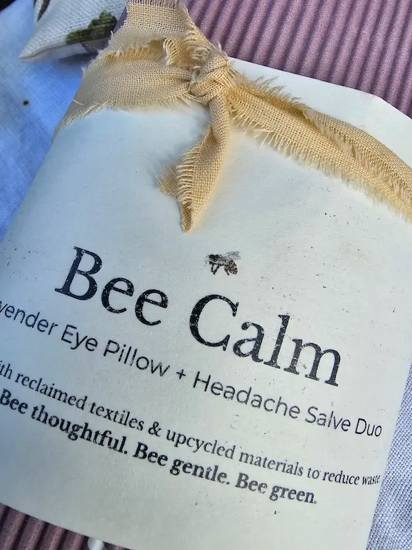Bee Calm product label and frayed cotton ribbon tied around lavender eye pillow and headache salve duo packaging.
