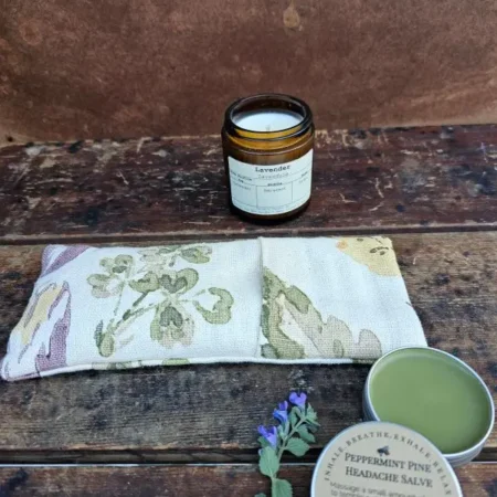 Bee-Calm-Hero Lavender eye pillow with peppermint pine headache salve and lavender candle arranged for a calming rest and relaxation scene.
