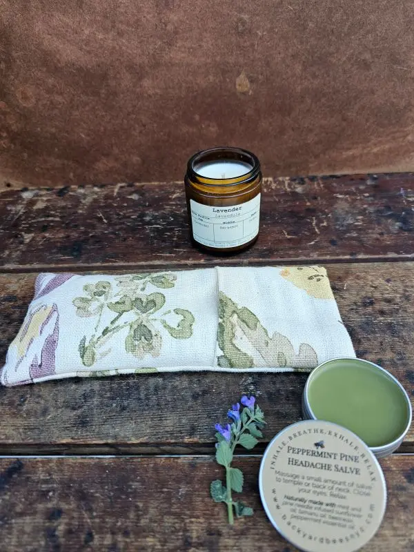 Lavender eye pillow with peppermint pine headache salve and lavender candle arranged for a calming rest and relaxation scene.