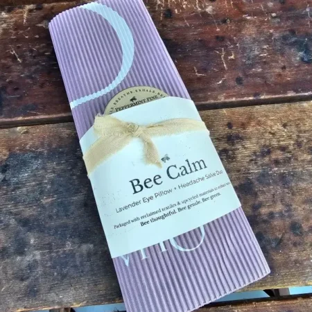 Bee-Calm-Wood Bee Calm lavender eye pillow and headache salve duo wrapped in reclaimed corrugated paper with cotton ribbon, displayed on rustic wood.
