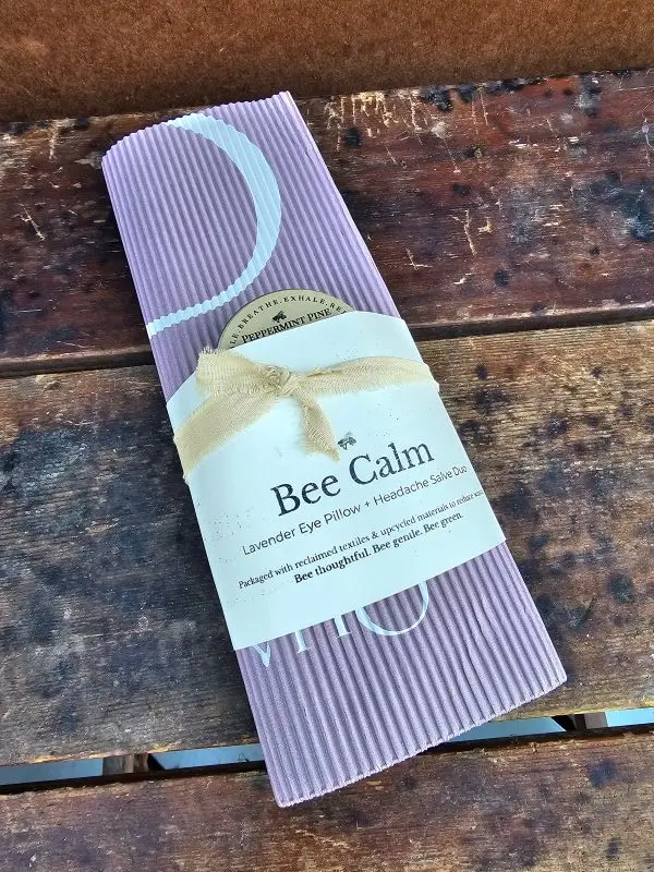 Bee Calm lavender eye pillow and headache salve duo wrapped in reclaimed corrugated paper with cotton ribbon, displayed on rustic wood.