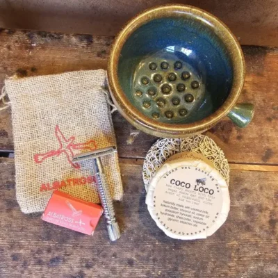 Stainless steel safety razor, shave brush, and Coco Loco shave bar on soap lift arranged on rustic wood grooming surface.