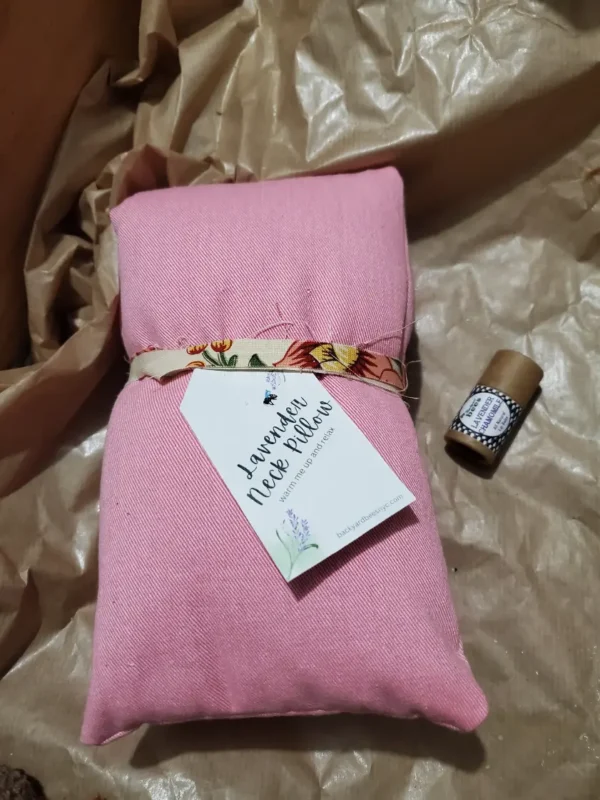 pink neck pillow on crinkled kraft brown paper, with a lavender lip balm tube