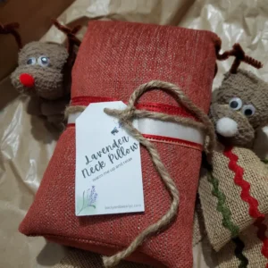 a deep red lavender neck pillow wrapped in ribbon with a tag and two washcloth reindeers