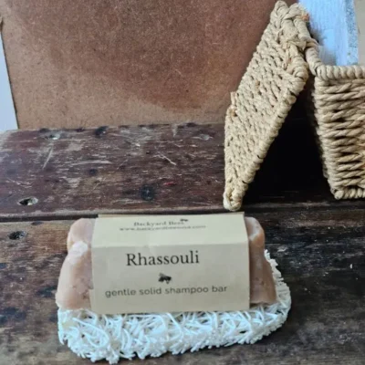 Rhassoul Shampoo Bar on white soap lift with basket of basekt towels behind on rustic setting