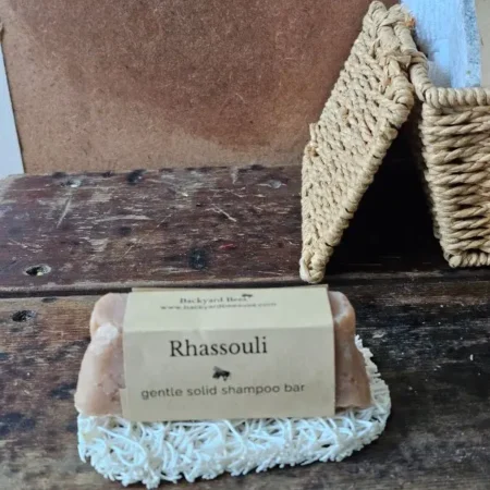 Rhassoul Shampoo Bar on white soap lift with basket of basekt towels behind on rustic setting