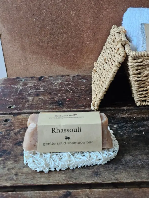 Rhassoul Shampoo Bar on white soap lift with basket of basekt towels behind on rustic setting
