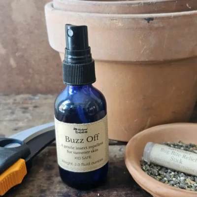 Buzz Off natural mosquito repellent on a garden table with terracotta pots, a deet-free insect repellent for outdoor living.