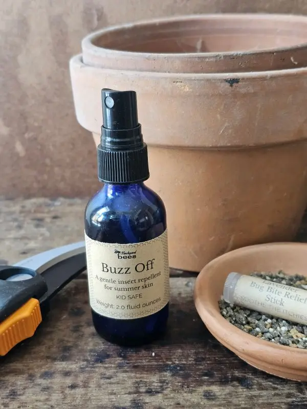 Buzz Off natural mosquito repellent on a garden table with terracotta pots, a deet-free insect repellent for outdoor living.