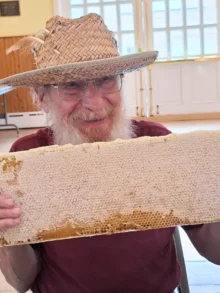 man in a farmers hat holding a frame of honey in honey harvesting workshop