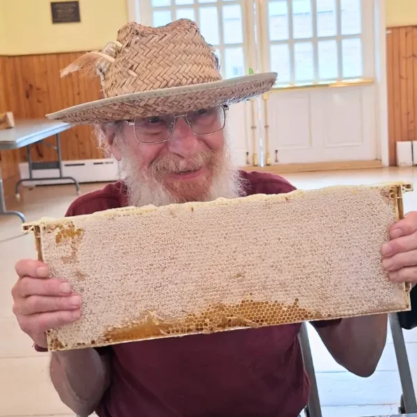 man in a farmers hat holding a frame of honey in honey harvesting workshop
