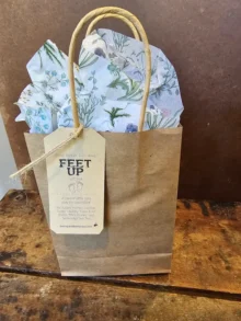 feet-up-hero Feet Up Gift Set in kraft gift bag with tag on rustic wood background.