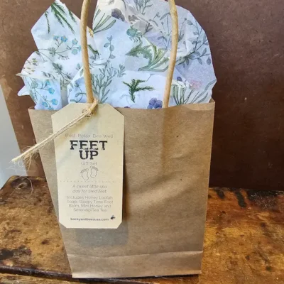 Feet Up Gift Set in kraft gift bag with tag on rustic wood background.
