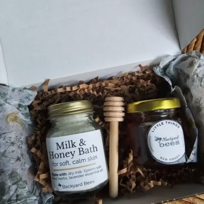 Inside the Milk & Honey Bath Ritual box: a jar of bath milk, raw honey, and a wooden honey dipper nestled in botanical tissue.