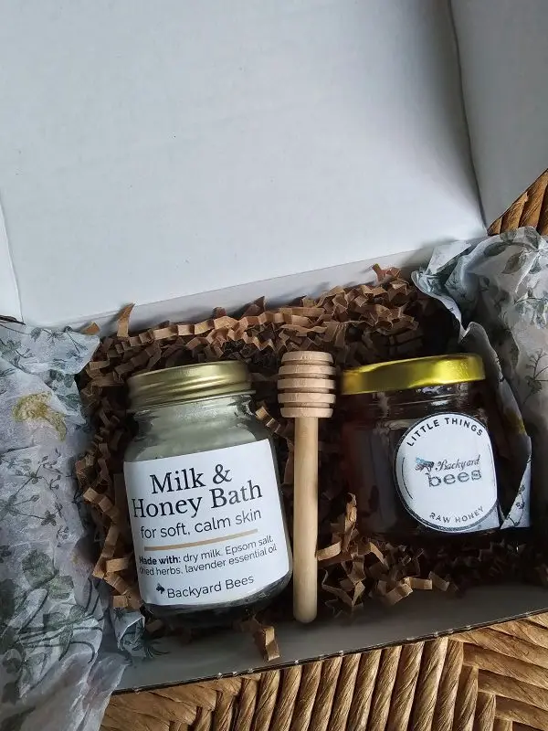 Inside the Milk & Honey Bath Ritual box: a jar of bath milk, raw honey, and a wooden honey dipper nestled in botanical tissue.