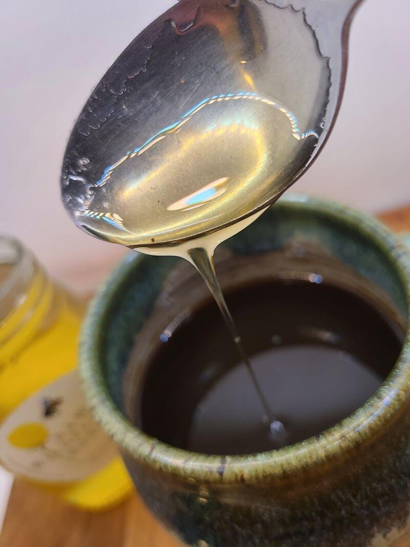 close up of honey on a spoon, dripping into a hot mug of coffee