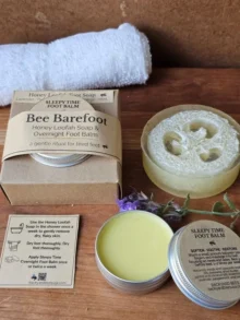Bee Barefoot Duo – Honey Loofah Soap + Sleepy Time Balm (Hero Image) Bee Barefoot Duo set with Honey Loofah Foot Soap, Sleepy Time Foot Balm, white towel, and greenery on a wooden board — calm natural flat lay