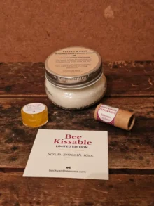 Flat lay of contents of Bee Kissable Gift Box on rustic wood table - Rosemary Mint Sugar Scrub, honey chamomile lip scrub, and Rose Kisses Lip Balm
