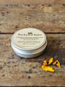 Backyard Balm calendula and comfrey salve in 2 oz tin with dried calendula petals on rustic wood surface