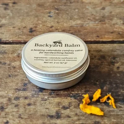 Backyard Balm Calendula Salve Backyard Balm calendula and comfrey salve in 2 oz tin with dried calendula petals on rustic wood surface