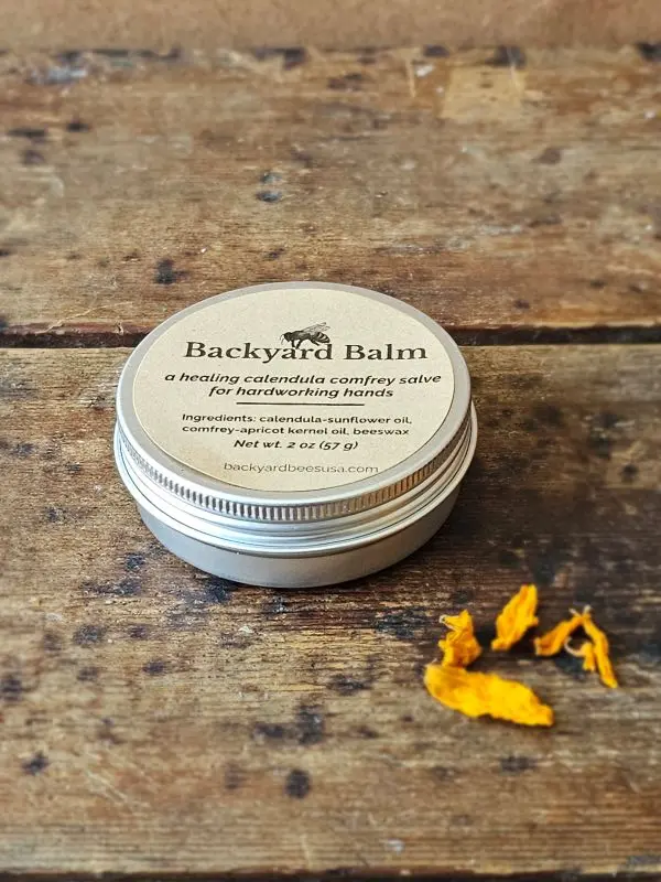 Backyard Balm Calendula Salve Backyard Balm calendula and comfrey salve in 2 oz tin with dried calendula petals on rustic wood surface