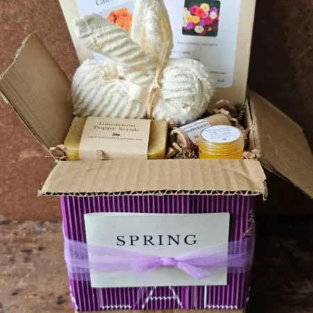 Spring Basket Open Open Spring Pollinator Basket gift box with purple corrugated wrap, cotton bunny washcloth, pollinator seed packets, botanical soap, and honey lip care inside recycled kraft box.