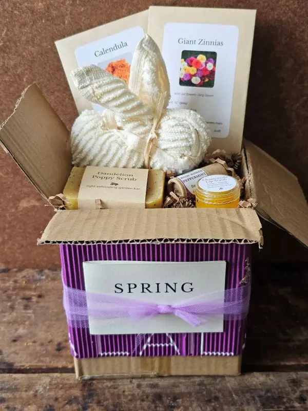 Open Spring Pollinator Basket gift box with purple corrugated wrap, cotton bunny washcloth, pollinator seed packets, botanical soap, and honey lip care inside recycled kraft box.