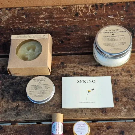 Natural spring skincare gift set with body scrub, foot care, and lip care products arranged on a wooden table
