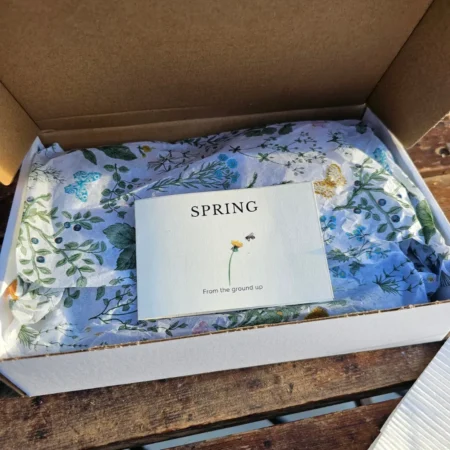 Spring skincare gift set with honey-based body scrub, foot balm, lip balm, and botanical packaging in an open box