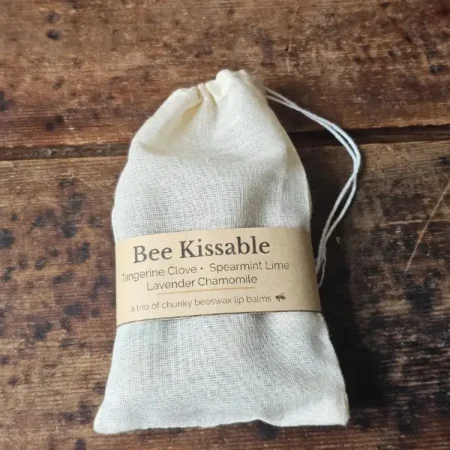 Bee Kissable Closed Bag drawstring muslin bag with Bee Kissable beeswax lip balm trio on weathered wood