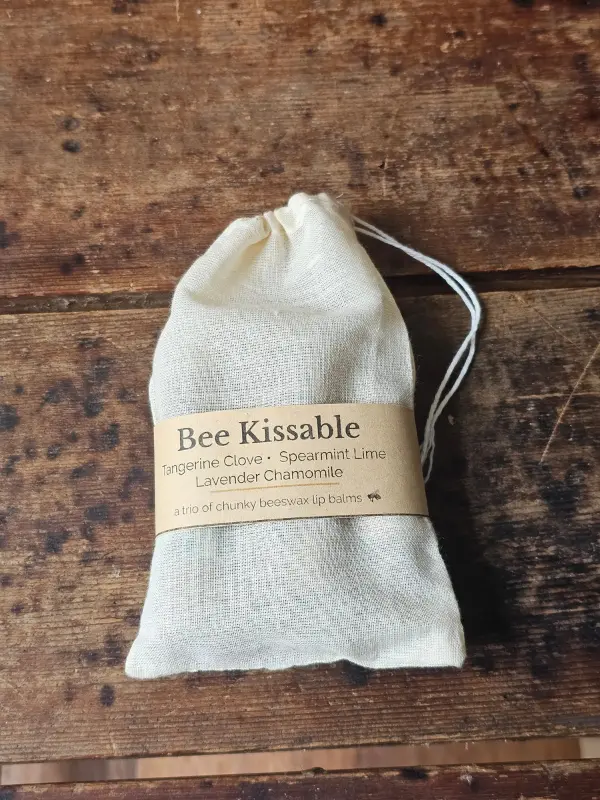 Bee Kissable Closed Bag drawstring muslin bag with Bee Kissable beeswax lip balm trio on weathered wood