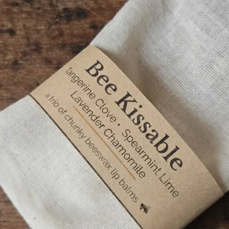 Bee Kissable Closeup Closeup of texture of muslin bag and kraft paper label for ecofriendly lip balm trio by Backyard Bees