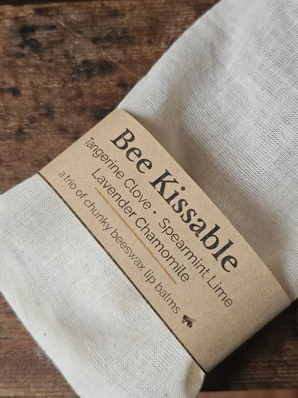 Bee Kissable Closeup Closeup of texture of muslin bag and kraft paper label for ecofriendly lip balm trio by Backyard Bees