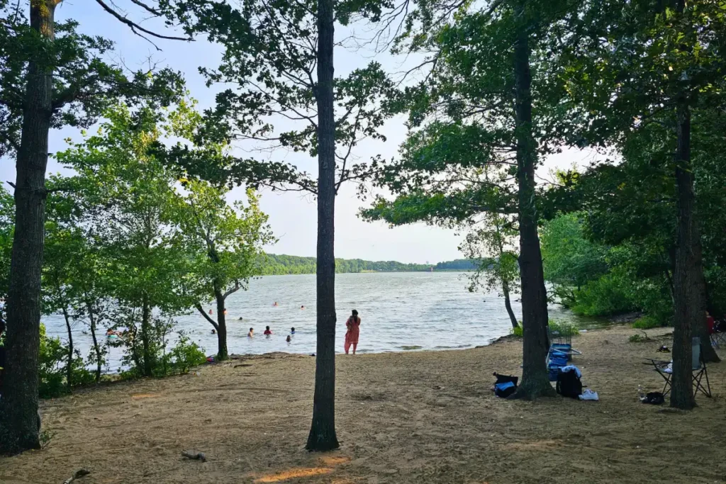 Families enjoying the sandy beach and lakefront at Hempstead Lake State Park during a summer evening.