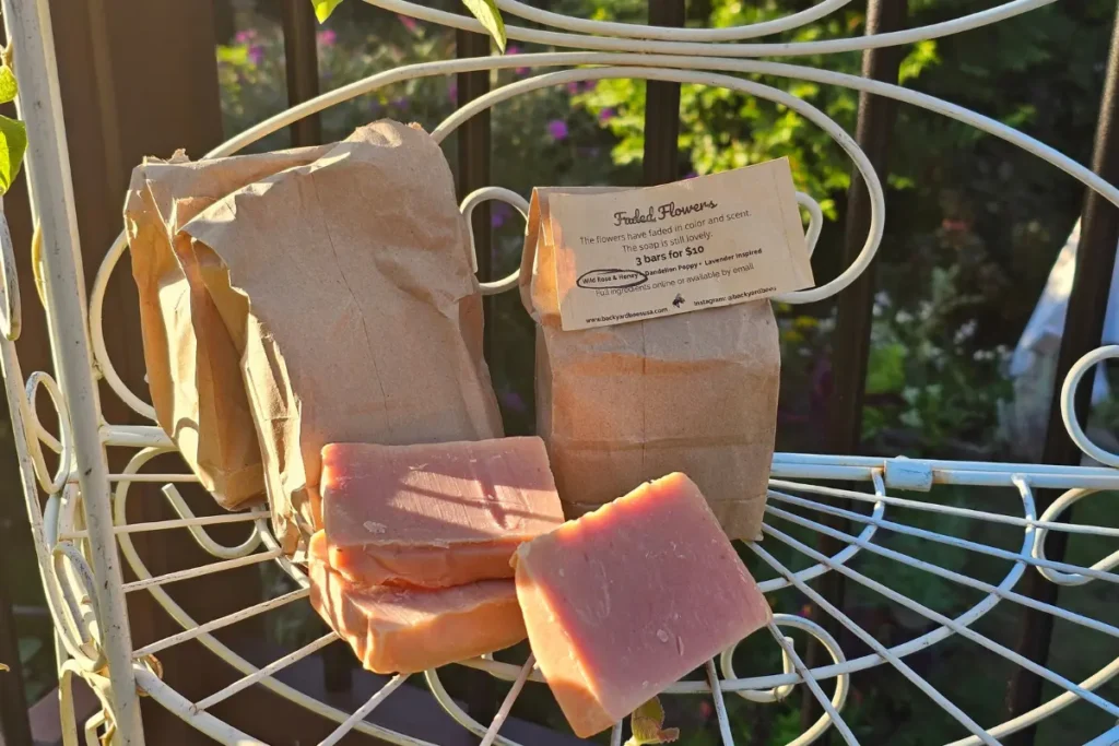 Faded Flowers kraft bags with assorted imperfect handmade soaps on outdoor metal plant stand.