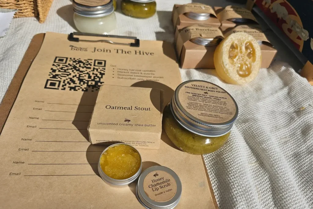 Backyard Bees body polish, orange lip scrub, and soap displayed on a farmers market sign-in sheet.